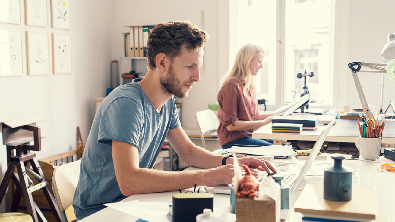 Man working on laptop in sunny office.