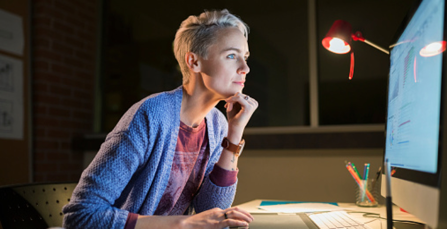 A women looking at her computer screen while working late at the office.