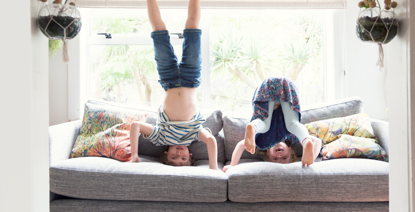 Two children doing headstands on a sofa.