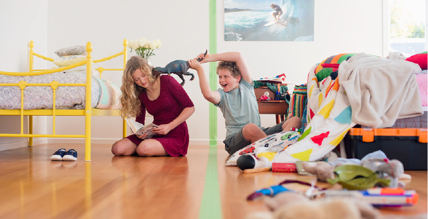 Siblings sharing a small space, with tape dividing two halves of a bedroom.